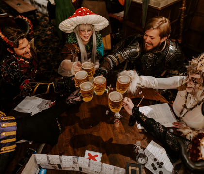 A group of cosplayers sitting around a table playing Dungeons and Dragons with beer.
