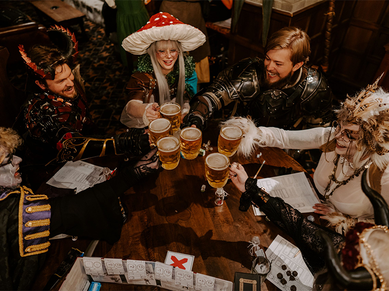 A group of cosplayers sitting around a table playing Dungeons and Dragons with beer.